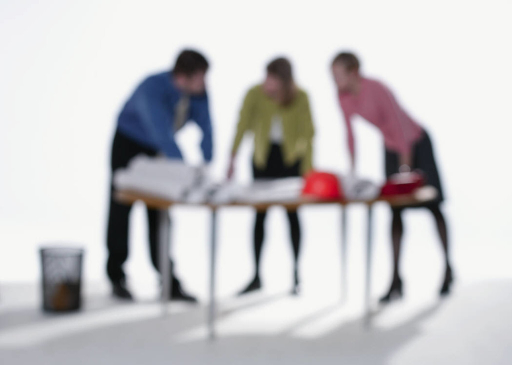 Blurry image of three people hunched over a desk full of paper work.