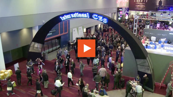video still of a hallway with purple carpet and gray walls filled with business people in suits under an arch saying, "International CES".