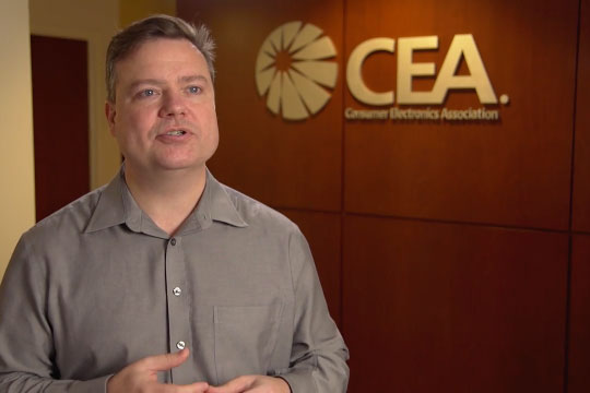 Photo of a man with a gray button down shirt in an office with the C E A logo.