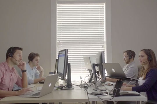 Photo of young professionals working on computers wearing head sets in a white room.